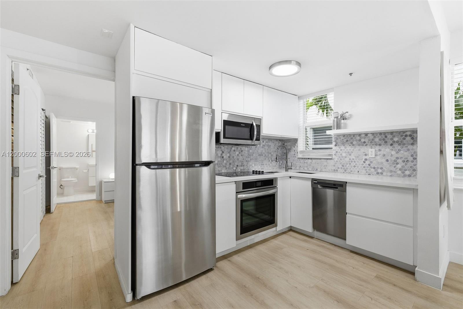 A modern kitchen features white cabinets, stainless steel appliances, and a hexagonal tile backsplash — 1550 Drexel Ave # 207, Miami Beach FL 33139, MIAMI BEACH, FL