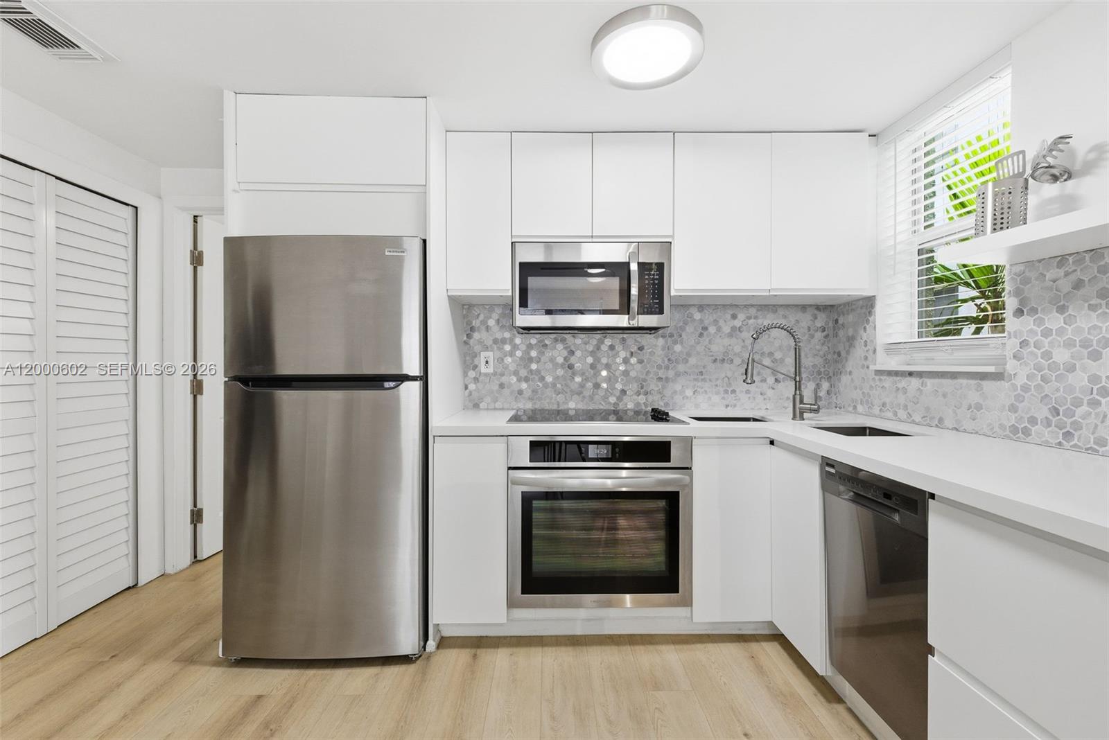 A modern kitchen features white cabinetry, stainless steel appliances, and a gray hexagonal tile backsplash — 1550 Drexel Ave # 207, Miami Beach FL 33139, MIAMI BEACH, FL