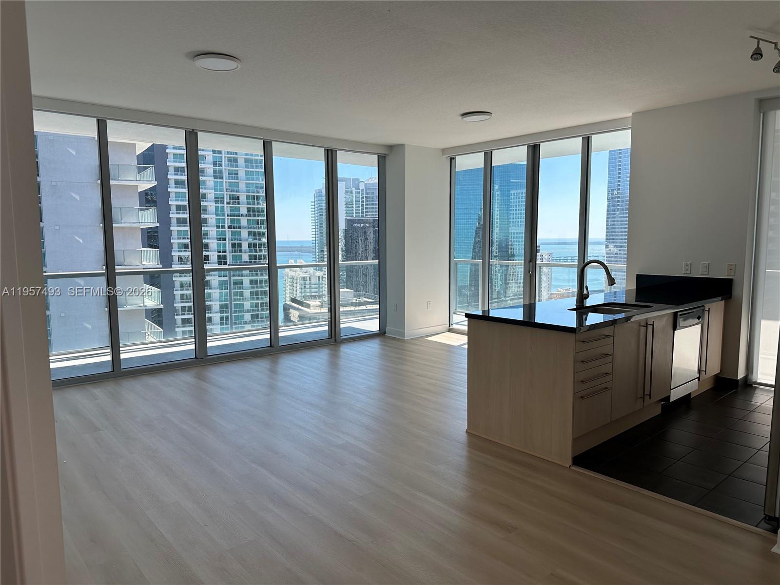 A modern apartment living area features light wood floors, a kitchen island, and floor-to-ceiling windows — 1111 SW 1st Ave, Miami FL 33130, MIAMI, FL