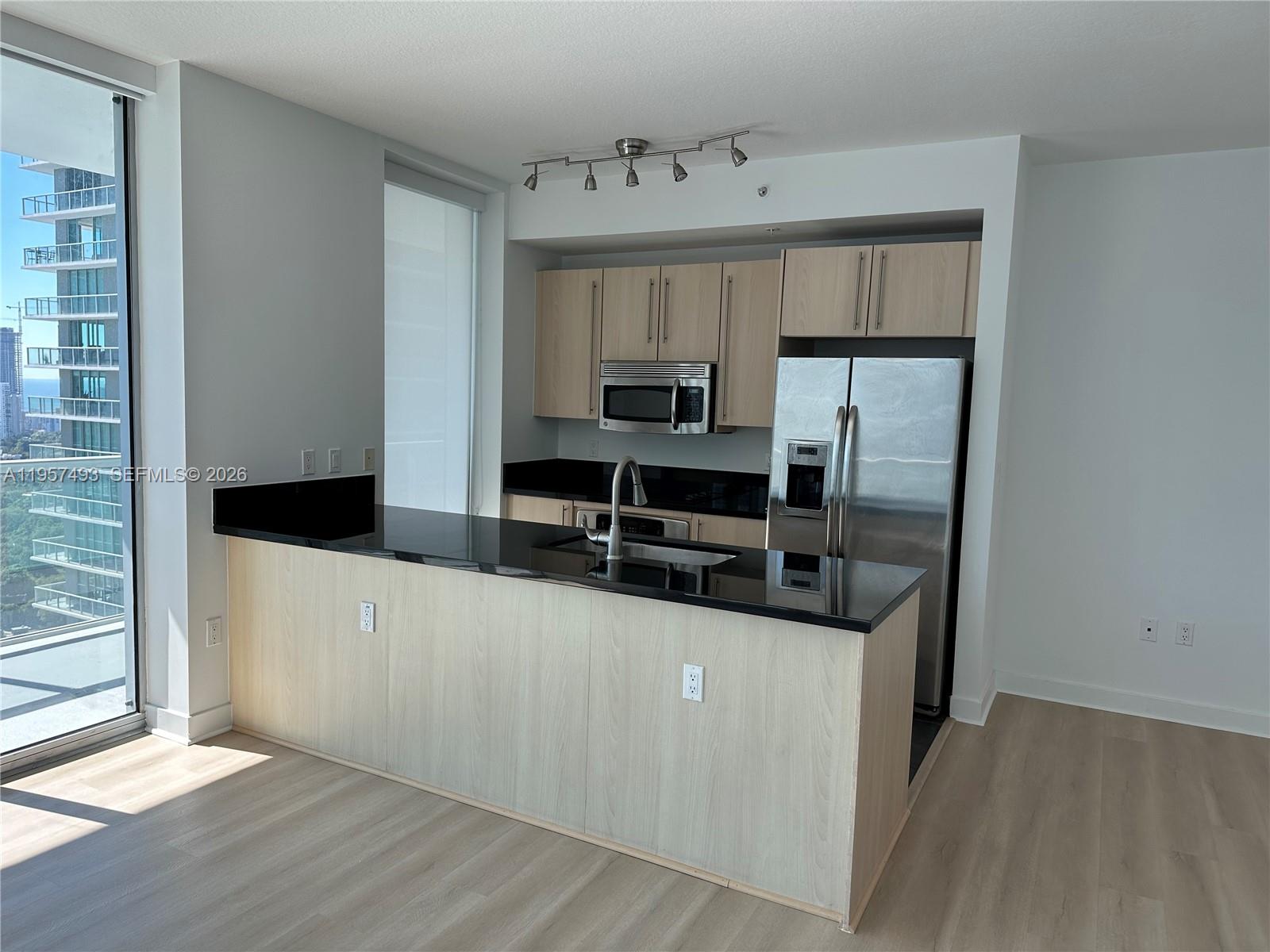 A modern kitchen features light wood cabinets, black countertops, stainless steel appliances, and floor-to-ceiling windows — 1111 SW 1st Ave, Miami FL 33130, MIAMI, FL