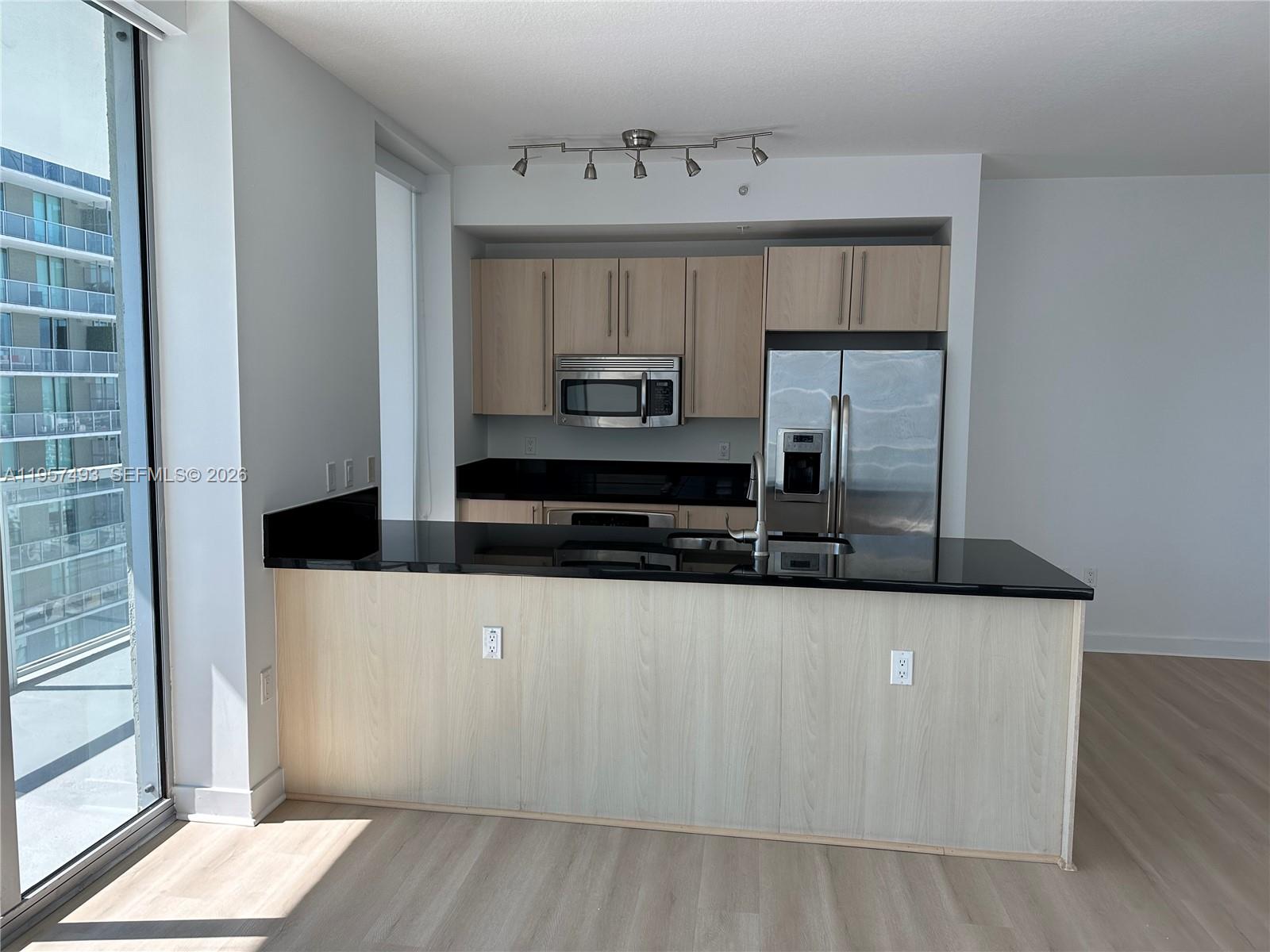 A kitchen features light wood cabinets, black countertops, stainless steel appliances, and a breakfast bar — 1111 SW 1st Ave, Miami FL 33130, MIAMI, FL