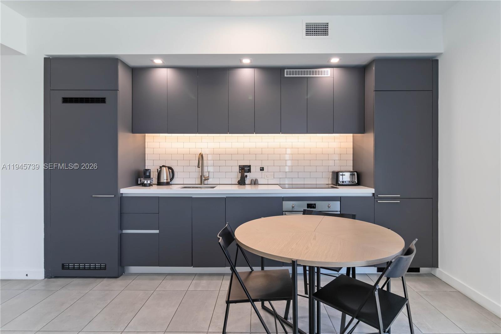 A modern kitchen features dark gray cabinetry, white subway tile backsplash, and a round table — 227 NE 2nd St # 2506, Miami FL 33132, MIAMI, FL