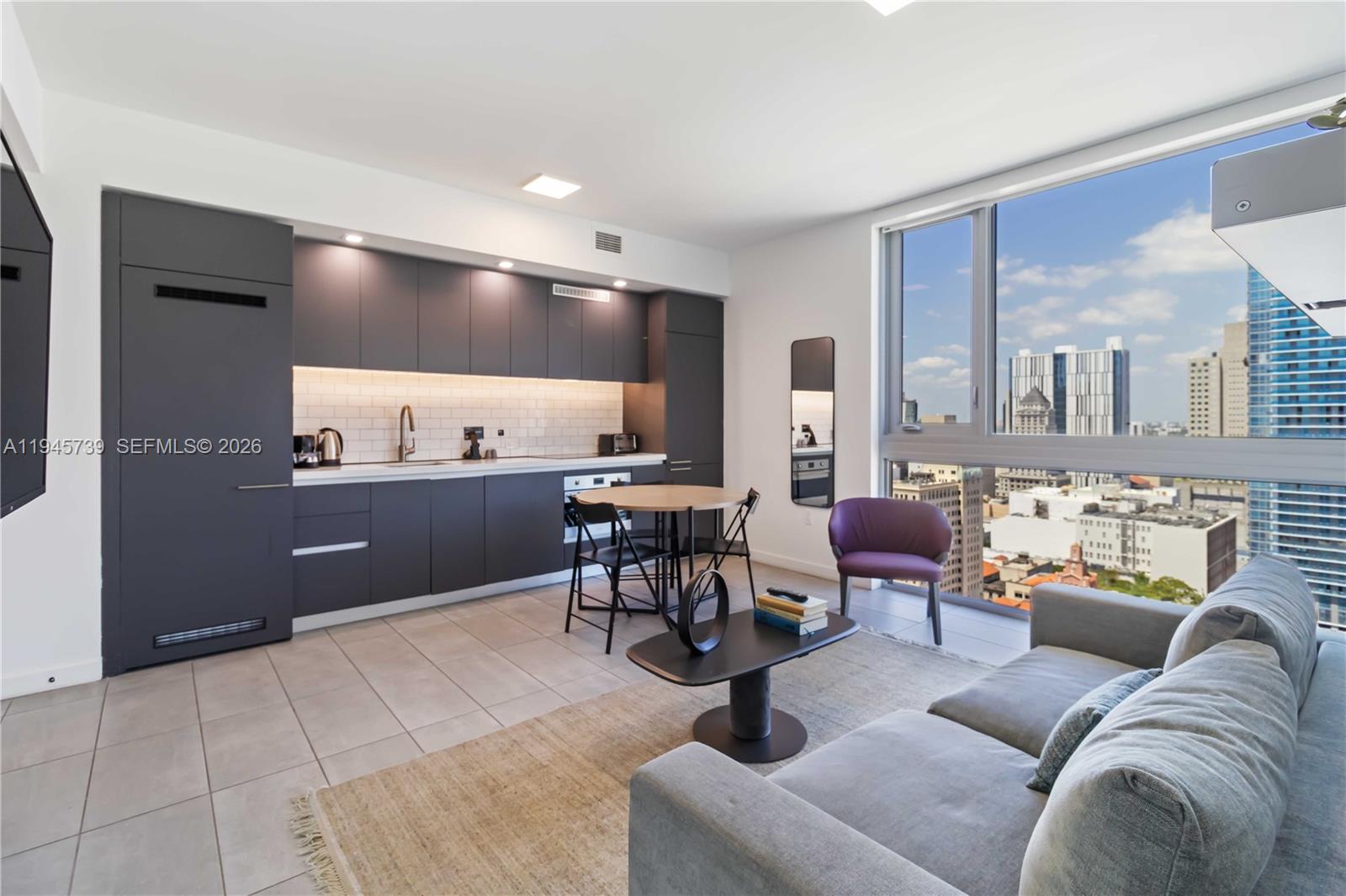 A modern studio apartment features a dark kitchen, dining area, and living room with city views — 227 NE 2nd St # 2506, Miami FL 33132, MIAMI, FL