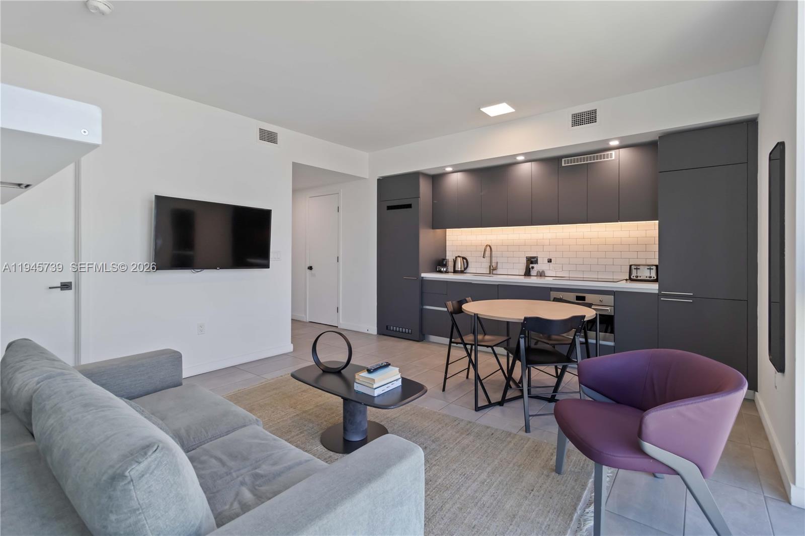 A modern studio apartment features a grey sofa, a dining table, and a dark kitchen — 227 NE 2nd St # 2506, Miami FL 33132, MIAMI, FL