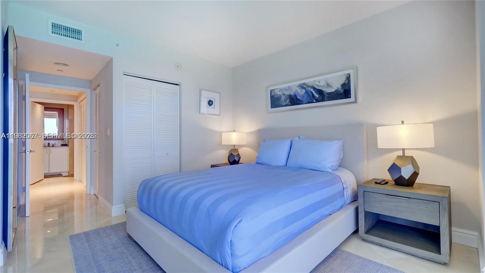 A bedroom features a bed with blue bedding, two nightstands with lamps, and a closet — 6365 Collins Ave # 3802, Miami Beach FL 33141, MIAMI BEACH, FL