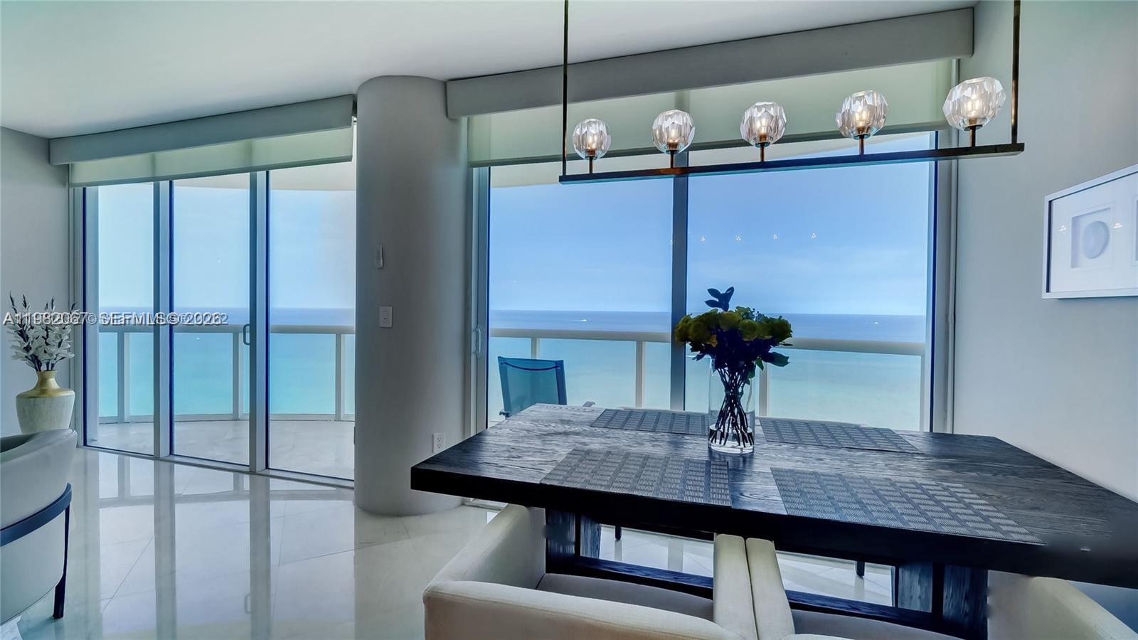 A dining area features a dark wood table, modern chandelier, and floor-to-ceiling ocean views — 6365 Collins Ave # 3802, Miami Beach FL 33141, MIAMI BEACH, FL