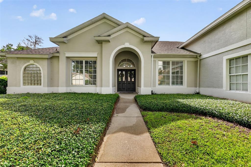 A concrete walkway leads to the front entrance of a single-story house with stucco siding — 9041 LAUREL RIDGE DRIVE, MOUNT DORA, FL