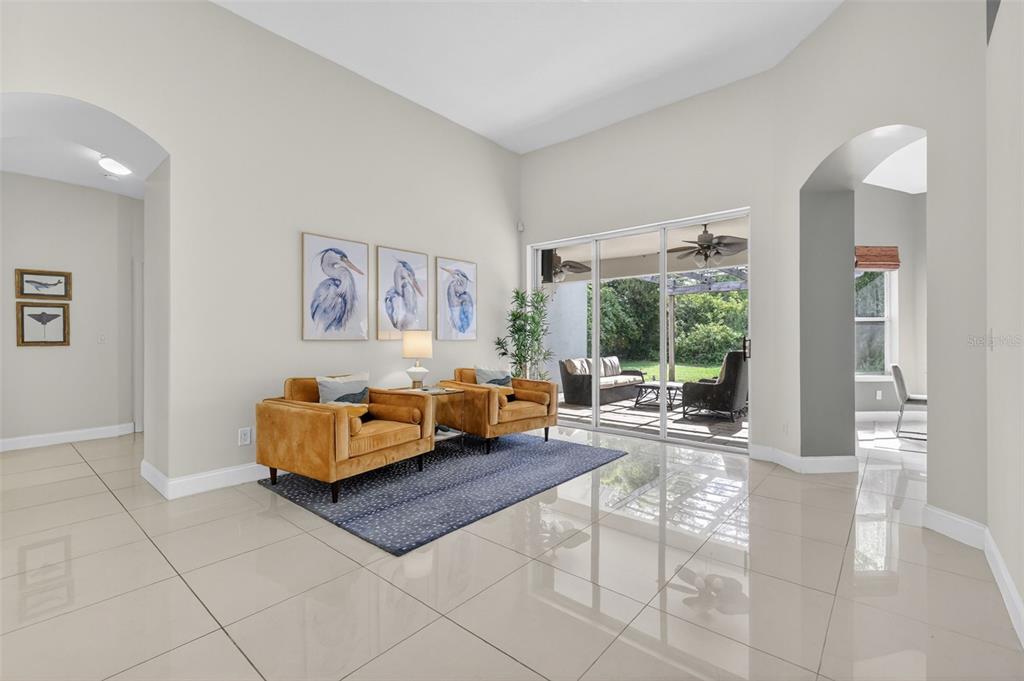 A bright living room features large floor tiles, two gold armchairs, and sliding glass doors — 9041 LAUREL RIDGE DRIVE, MOUNT DORA, FL