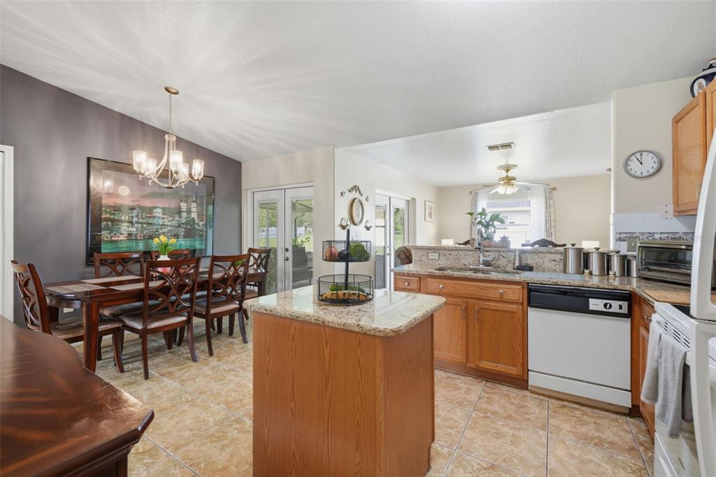A kitchen with wood cabinets and a granite island opens to a dining area — 1029 DUDLEY DRIVE, KISSIMMEE, FL