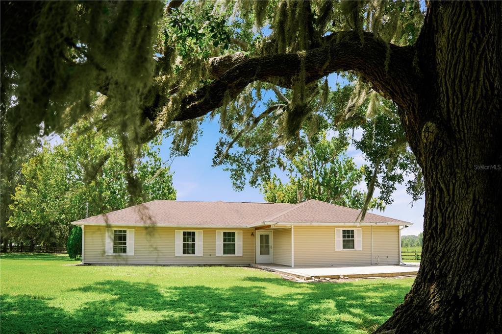 A single-story house with light-colored siding stands behind a large, moss-covered oak tree — 3430 WESTSHORE DRIVE, ST CLOUD, FL