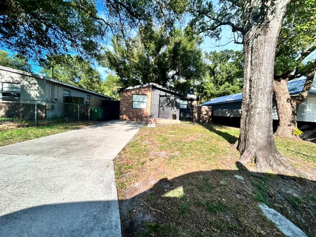 A small, single-story brick house with a concrete driveway and a large tree in front — 4607 N 35TH STREET, TAMPA, FL
