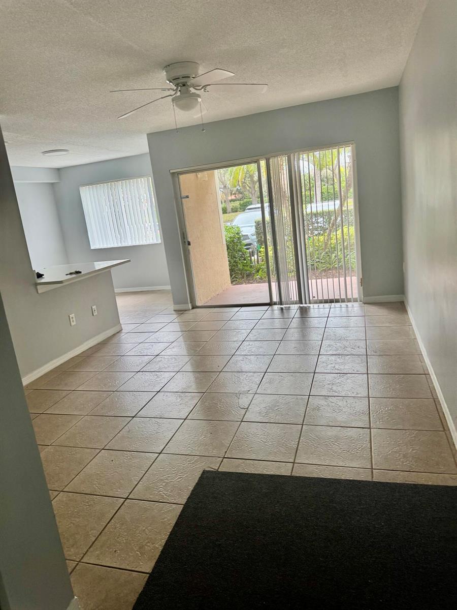 An open-concept living area features light-colored tile flooring, a ceiling fan, and sliding glass doors — 1670 N 42nd Circle # 105, Vero Beach FL 32967, VERO BEACH, FL