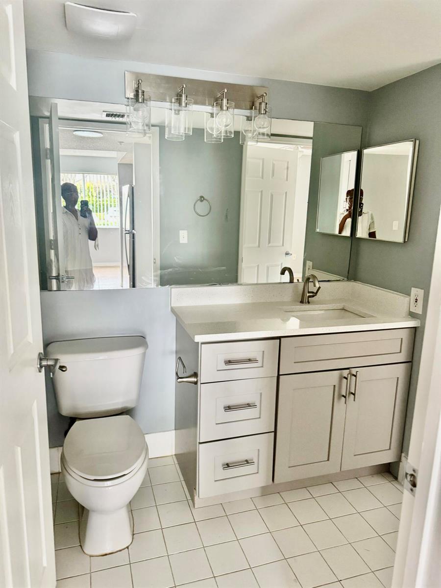 A bathroom features a gray vanity with a white countertop, a toilet, and a large mirror — 1670 N 42nd Circle # 105, Vero Beach FL 32967, VERO BEACH, FL