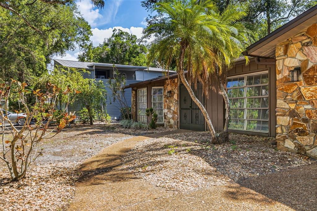 A stone-clad house exterior features a palm tree, a gravel yard, and a metal-roofed structure — 2749 GREENDALE DRIVE, SARASOTA, FL