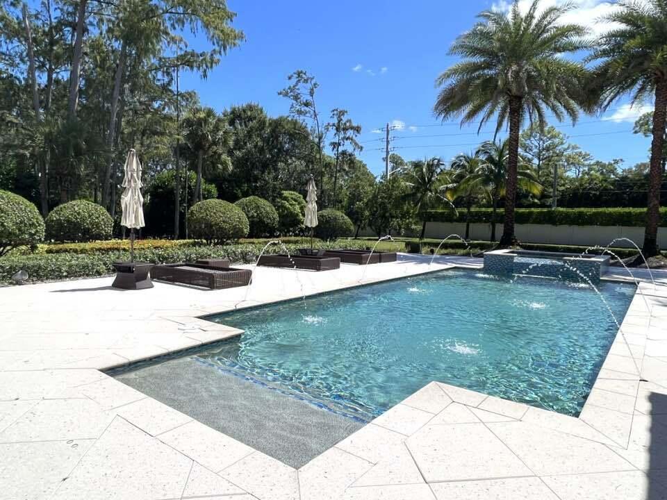 A rectangular swimming pool with fountains and a spa sits on a stone patio — 13550 Greentree Trail, Wellington FL 33414, WELLINGTON, FL