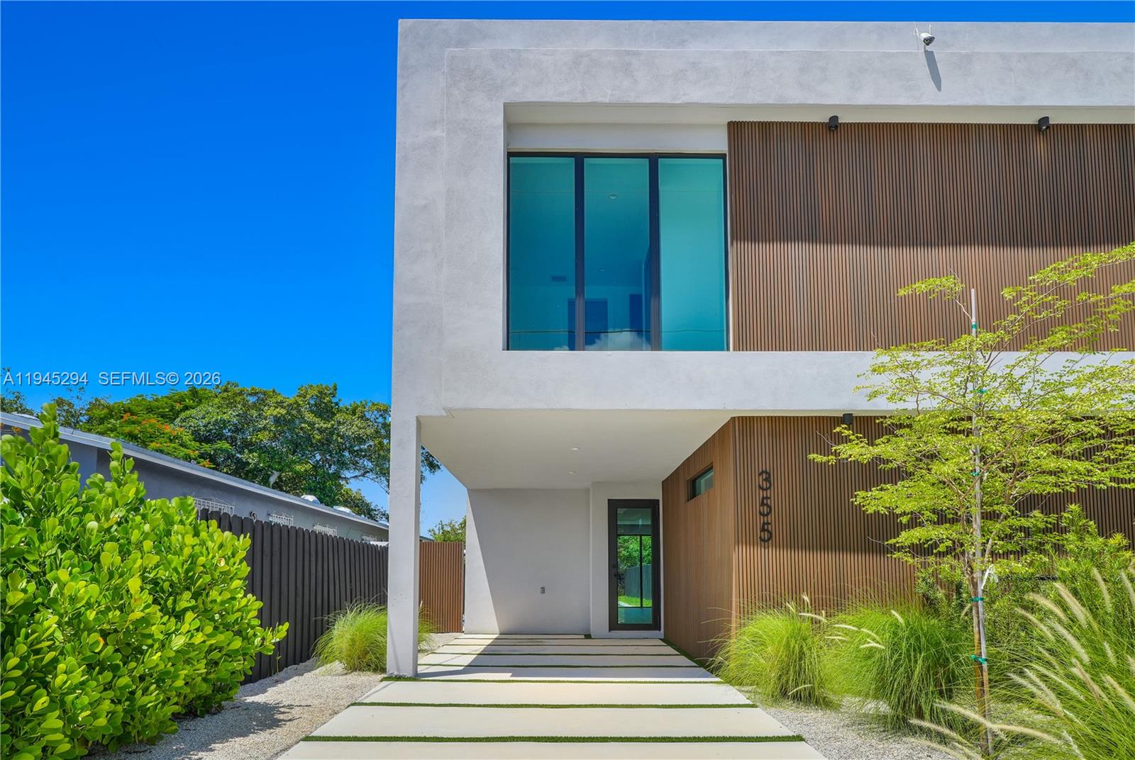 A modern two-story house features a white stucco facade, wood-slatted siding, and a paved driveway — 355 NW 50th St, Miami FL 33127, MIAMI, FL