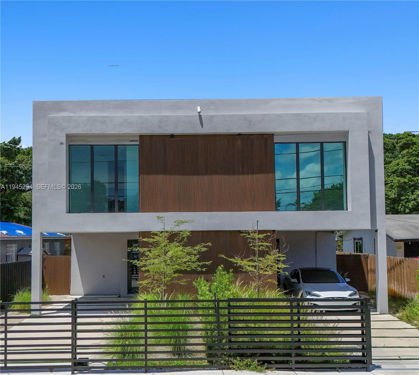 A modern two-story house features a gray facade with wood-slat accents and a metal fence — 355 NW 50th St, Miami FL 33127, MIAMI, FL