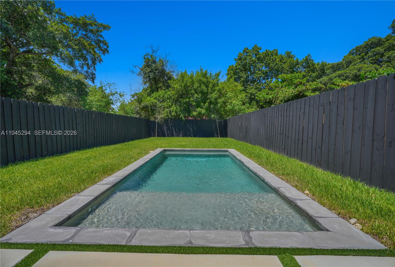 A rectangular swimming pool with a tanning ledge sits in a fenced grassy backyard — 355 NW 50th St, Miami FL 33127, MIAMI, FL