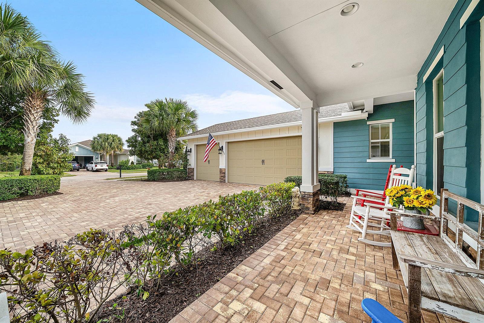 A covered porch with a brick floor features rocking chairs and a view of a driveway — 1107 Timber Reap Trail, Loxahatchee FL 33470, LOXAHATCHEE, FL
