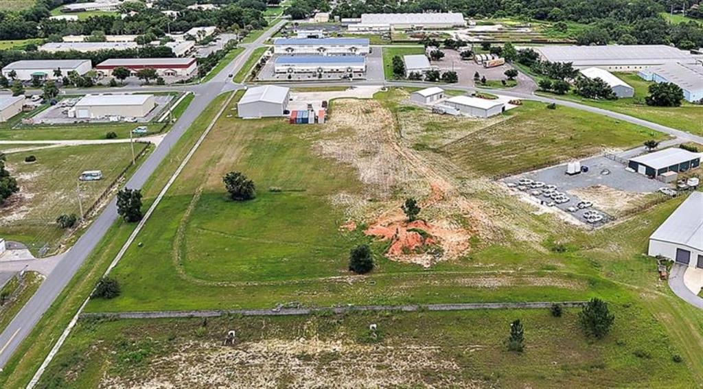 An aerial view shows a vacant, grassy lot surrounded by industrial buildings and paved roads — 1721 LEESBURG COMMONS COURT, LEESBURG, FL
