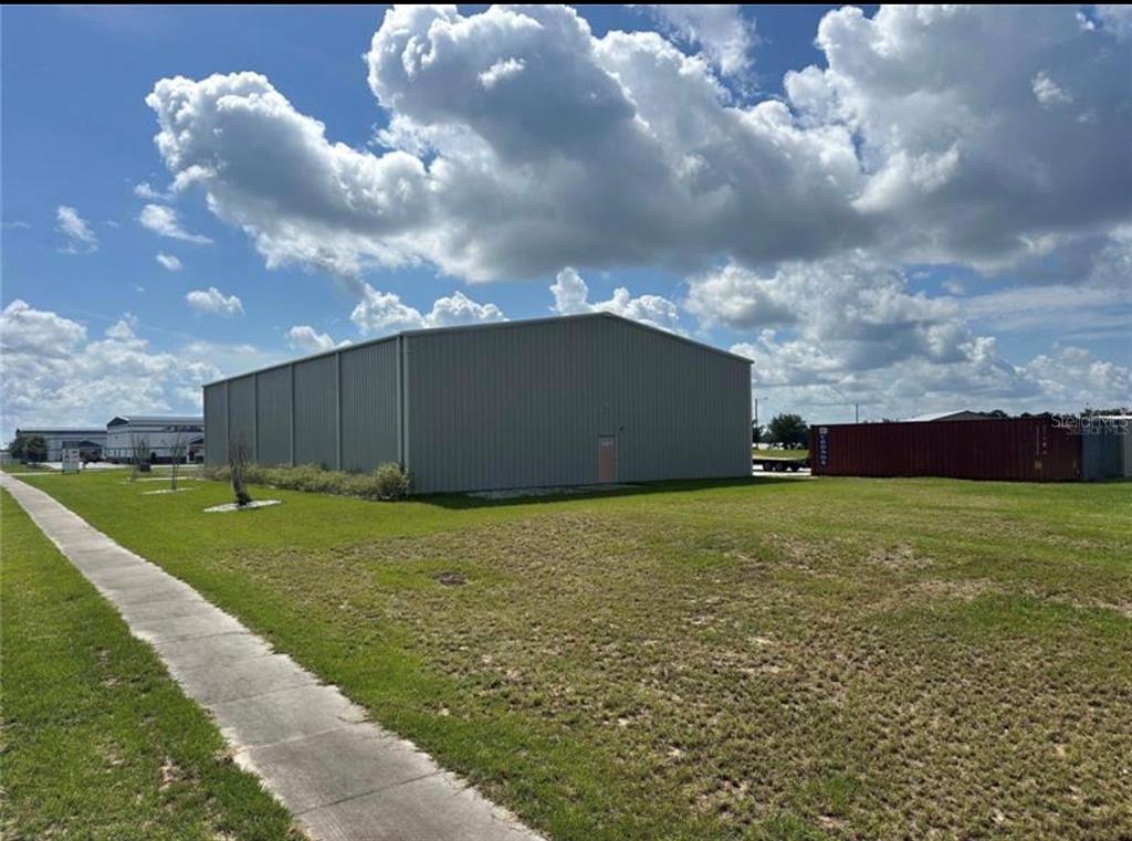 A metal warehouse building sits on a grassy lot next to a concrete sidewalk — 1721 LEESBURG COMMONS COURT, LEESBURG, FL