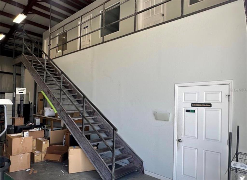 A warehouse interior features a metal staircase leading to an upper-level office area — 1721 LEESBURG COMMONS COURT, LEESBURG, FL