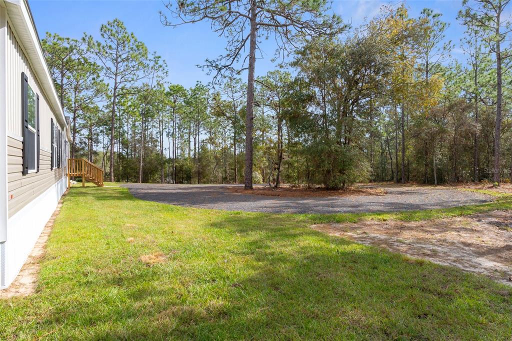 A view of a grassy yard next to a house with a gravel driveway — 6149 LA PINE ROAD, BROOKSVILLE, FL