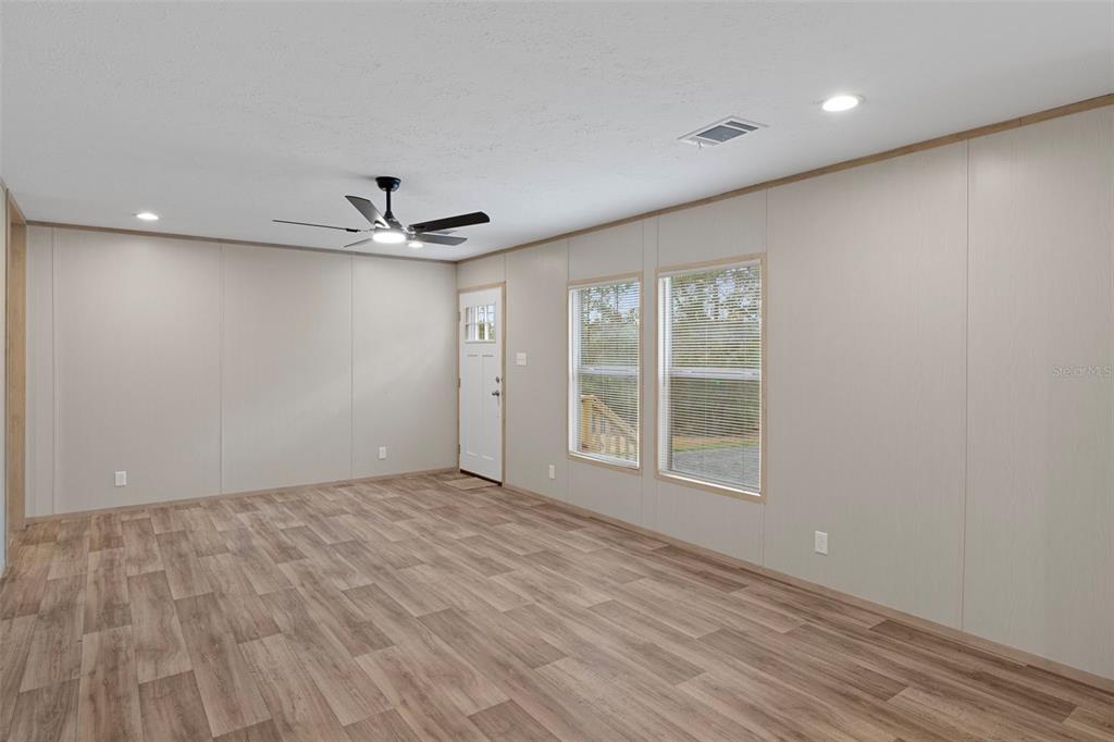 An empty room with light wood-look flooring, beige paneled walls, and a ceiling fan — 6149 LA PINE ROAD, BROOKSVILLE, FL