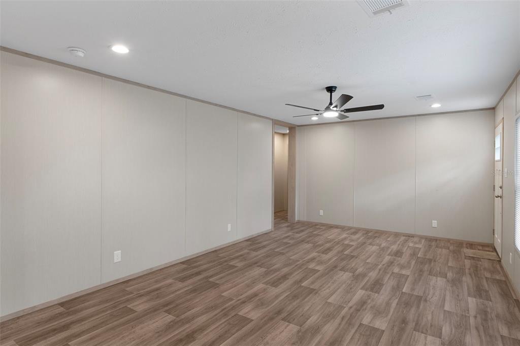 An empty room with light-colored paneled walls, wood-look flooring, and a ceiling fan — 6149 LA PINE ROAD, BROOKSVILLE, FL