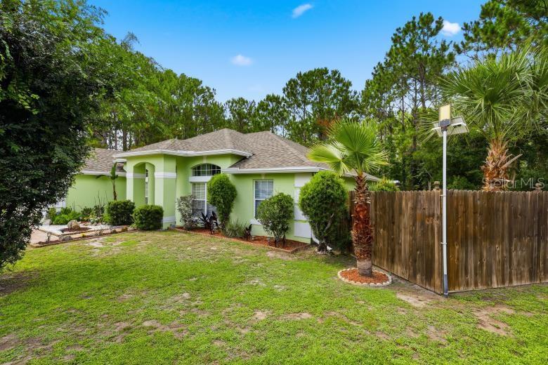 A light green house with a shingled roof stands behind a wooden fence and lawn — 18 BURTON PLACE, PALM COAST, FL