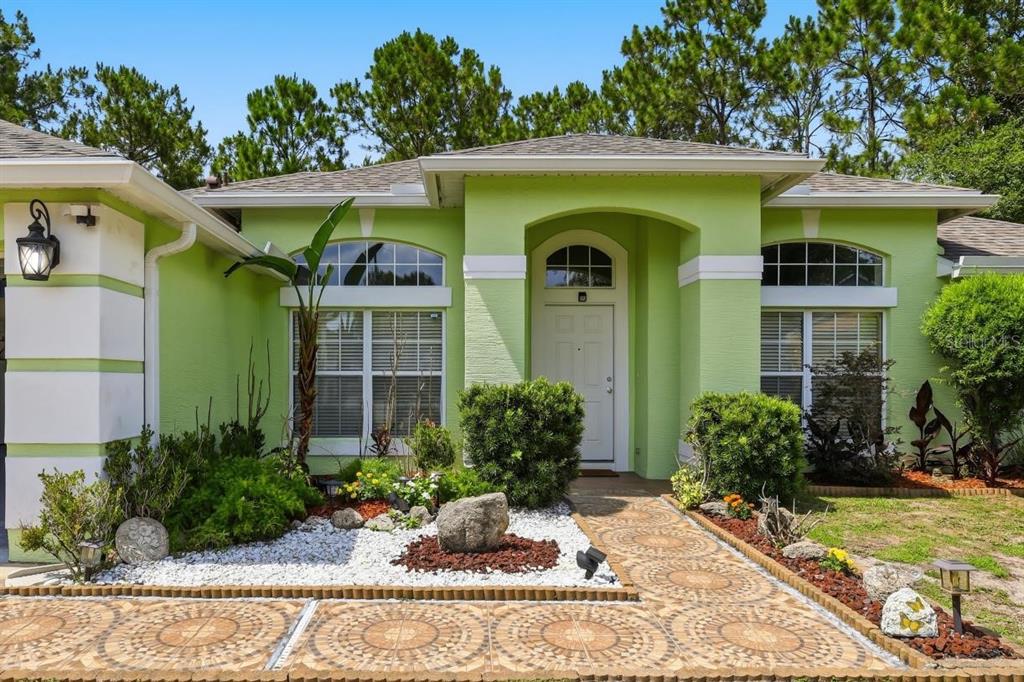 A lime green house exterior features a tiled walkway, white trim, and landscaped front garden — 18 BURTON PLACE, PALM COAST, FL