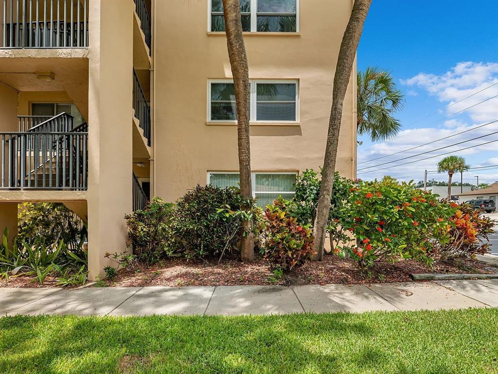 A tan multi-story apartment building exterior features a balcony, landscaping, and two palm trees — 2525 W BAY DRIVE UNIT A16, LARGO, FL