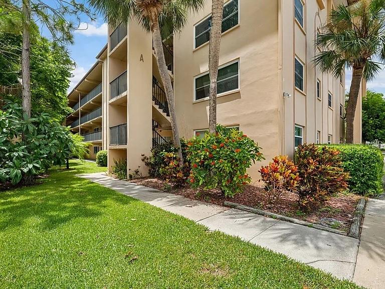 A multi-story apartment building exterior features a concrete walkway, landscaping, and palm trees — 2525 W BAY DRIVE UNIT A16, LARGO, FL