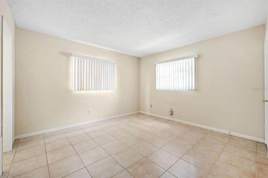 An empty bedroom with beige walls, tile flooring, and two windows with vertical blinds — 2525 W BAY DRIVE UNIT A16, LARGO, FL