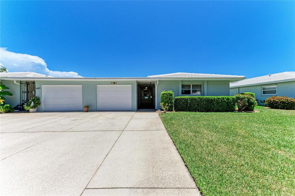 A light blue single-story house features a two-car garage, a concrete driveway, and green landscaping — 6905 9TH AVENUE W UNIT 6905, BRADENTON, FL
