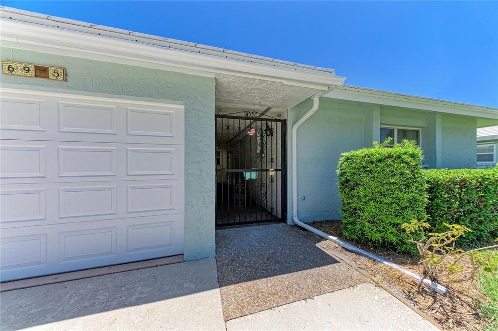 The exterior of a house features a white garage door, a gated entryway, and landscaping — 6905 9TH AVENUE W UNIT 6905, BRADENTON, FL