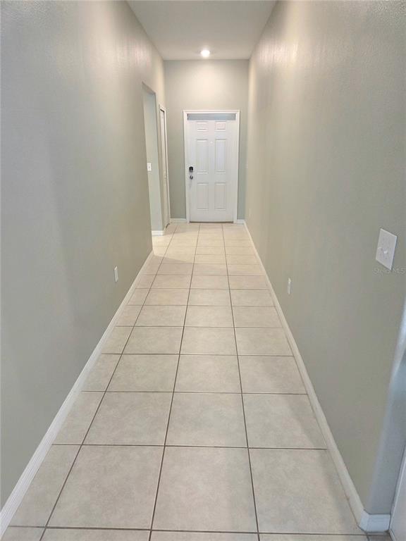 A long, narrow hallway with light-colored tile flooring and neutral walls leads to a white door — 10316 SHADY PRESERVE DRIVE, RIVERVIEW, FL