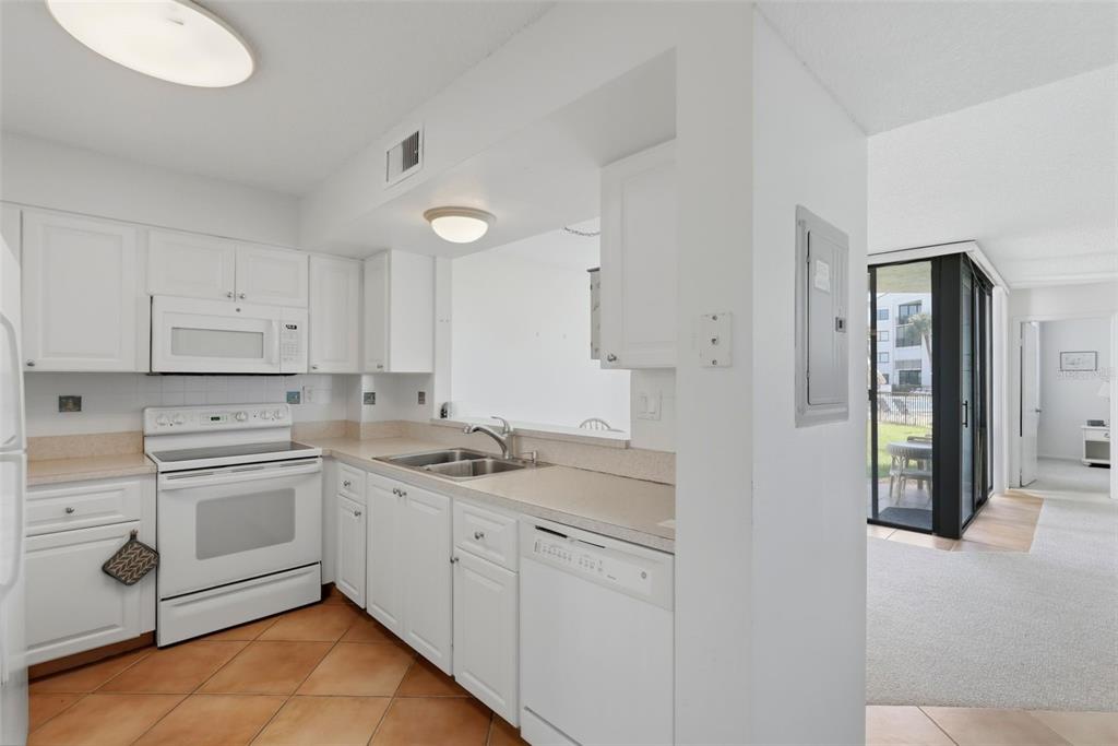 A kitchen with white cabinets, white appliances, and tile flooring opens to a living area — 5729 PUERTA DEL SOL BOULEVARD S UNIT 186, ST PETERSBURG, FL
