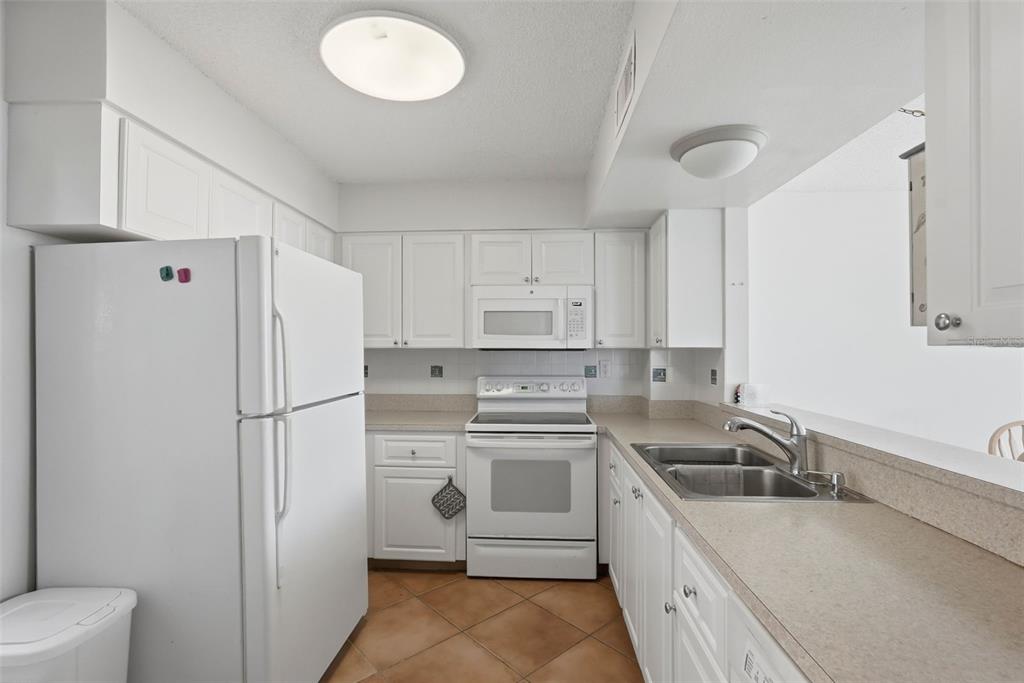 A kitchen with white cabinets, white appliances, a double sink, and tan tile flooring — 5729 PUERTA DEL SOL BOULEVARD S UNIT 186, ST PETERSBURG, FL