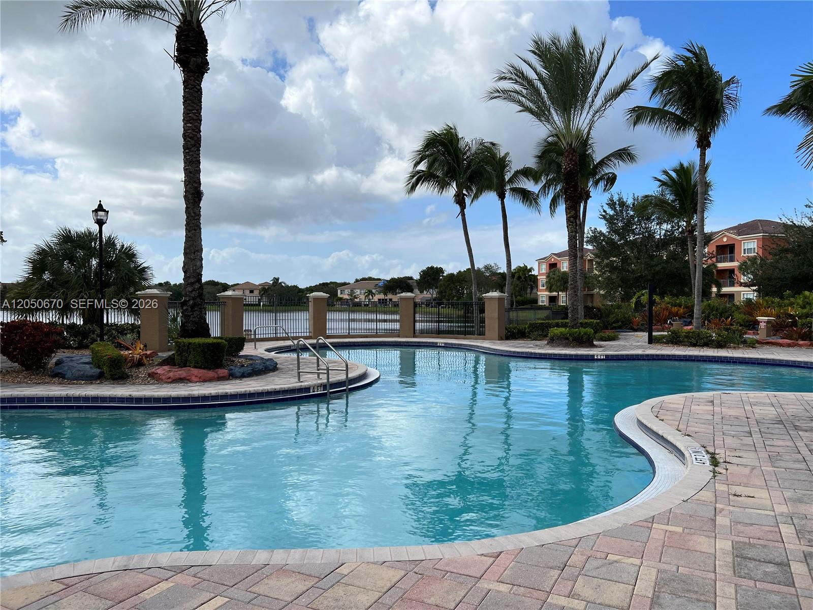 A swimming pool with a brick deck and palm trees overlooks a lake and buildings — 4600 SW 160th Ave # 619, Miramar FL 33027, MIRAMAR, FL