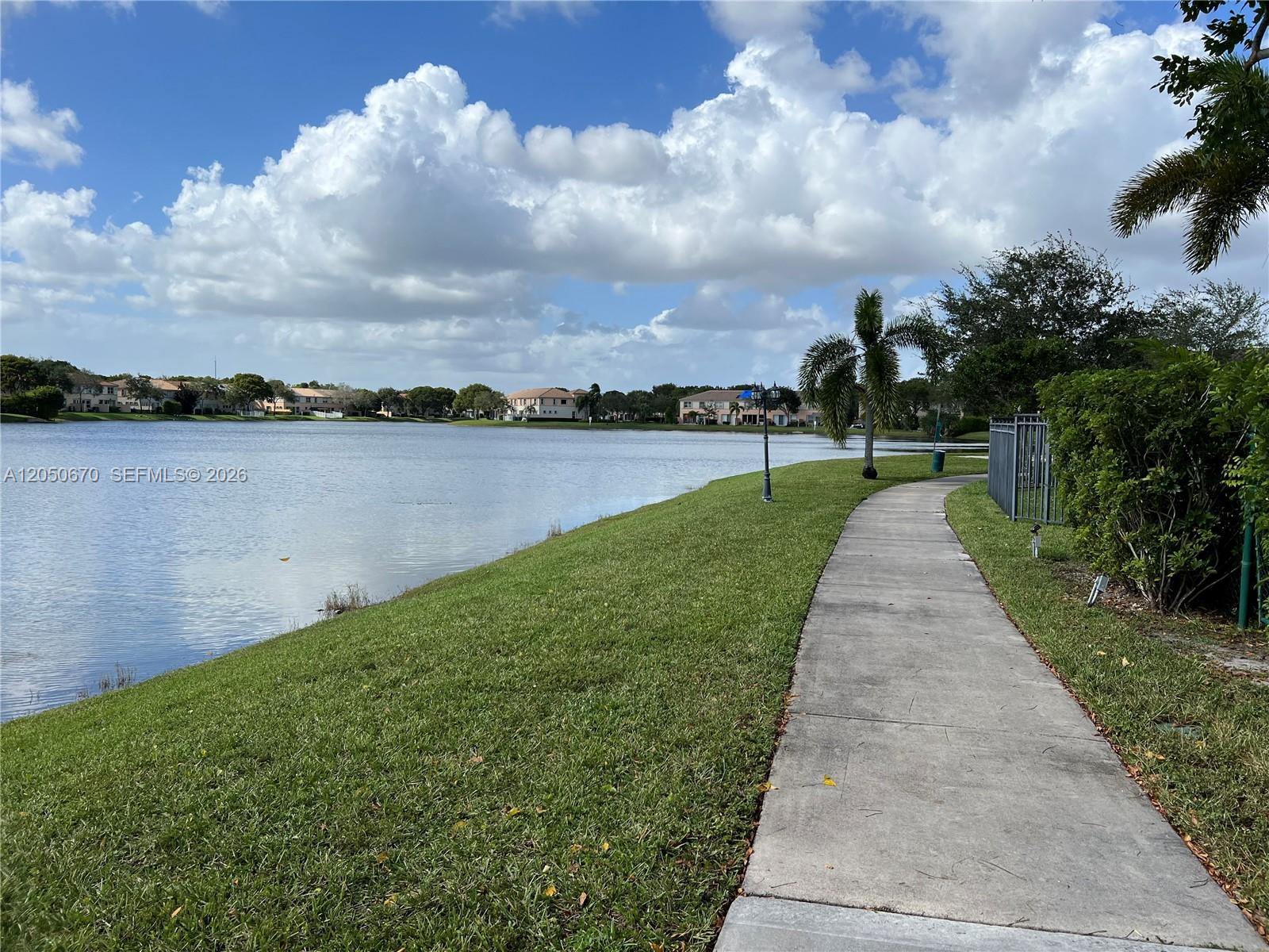 A concrete pathway runs along a grassy bank beside a large lake — 4600 SW 160th Ave # 619, Miramar FL 33027, MIRAMAR, FL