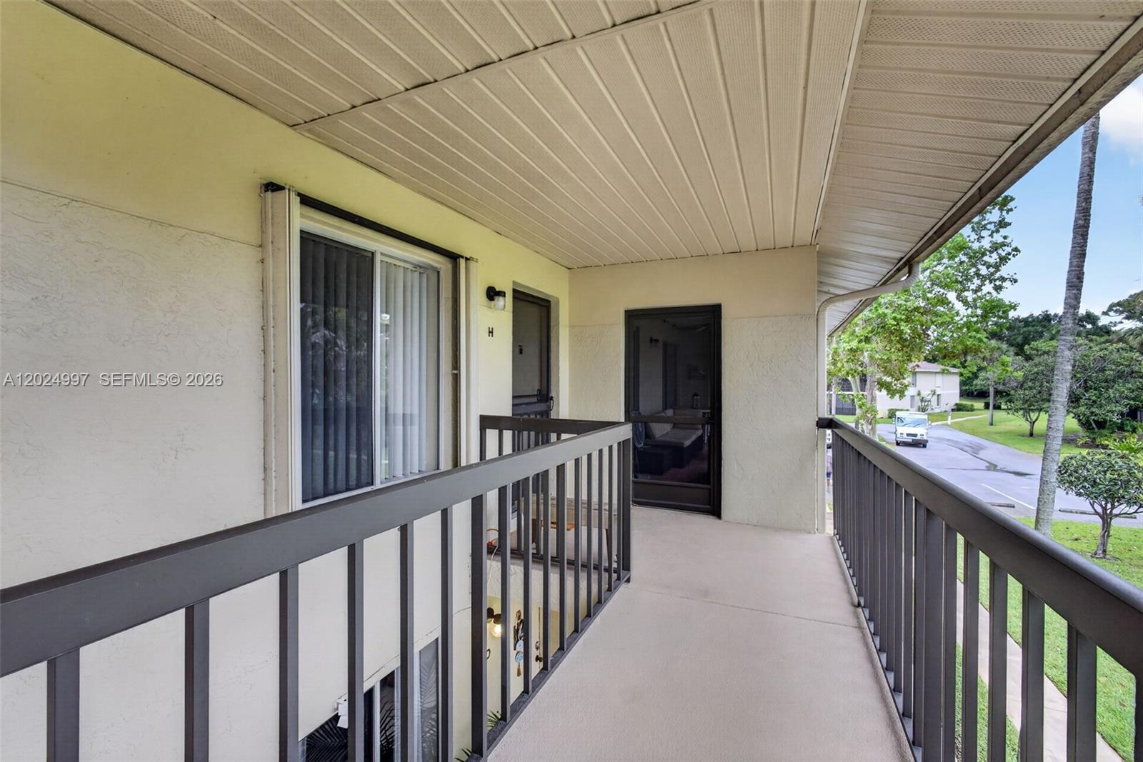 An exterior walkway features a beige stucco wall, a metal railing, and two entry doors — 6555 Chasewood Dr # H, Jupiter FL 33458, JUPITER, FL