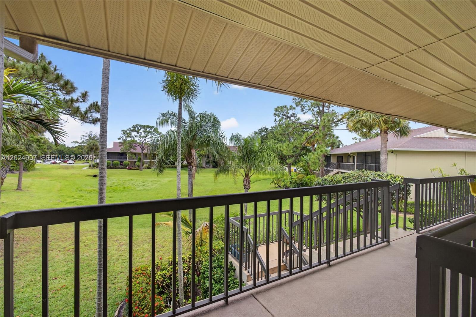 A covered balcony with a dark metal railing overlooks a grassy lawn and palm trees — 6555 Chasewood Dr # H, Jupiter FL 33458, JUPITER, FL