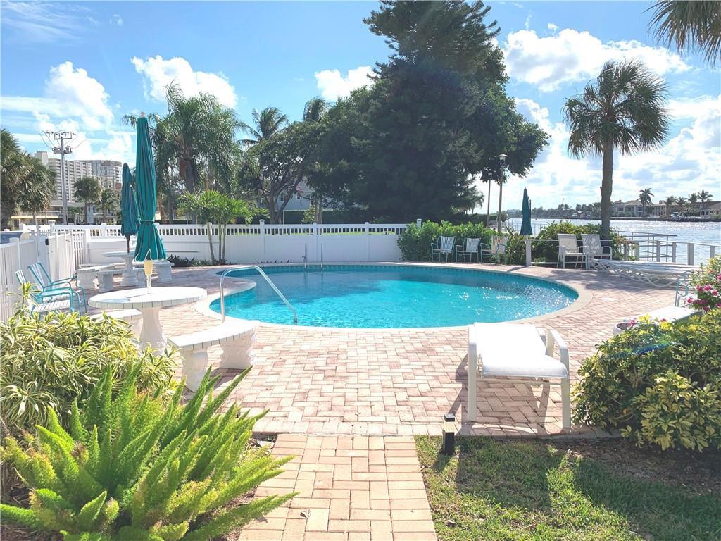 A round swimming pool sits on a brick patio overlooking a canal with palm trees — 1201 N Riverside Drive # 12b, Pompano Beach FL 33062, POMPANO BEACH, FL