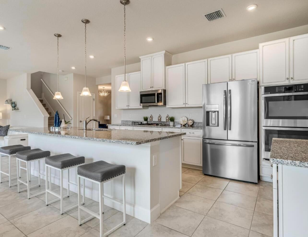 A kitchen with white cabinets, granite countertops, stainless steel appliances, and a breakfast bar with stools — 1224 Harvester Crossing, Loxahatchee FL 33470, LOXAHATCHEE, FL