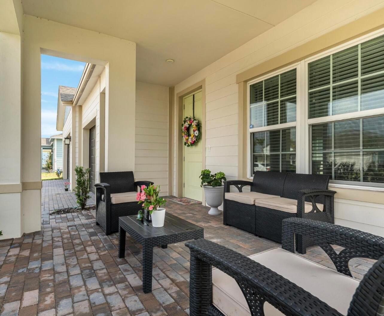 A covered brick patio features black wicker furniture and a light green front door — 1224 Harvester Crossing, Loxahatchee FL 33470, LOXAHATCHEE, FL