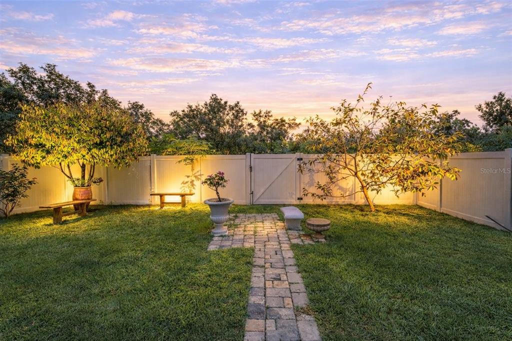 A backyard features a stone path, a white fence, trees, and benches at sunset — 5206 WILLOW BREEZE WAY, PALMETTO, FL