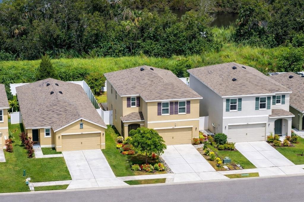 An aerial view of three suburban houses with driveways and lawns bordering a wooded area — 5206 WILLOW BREEZE WAY, PALMETTO, FL