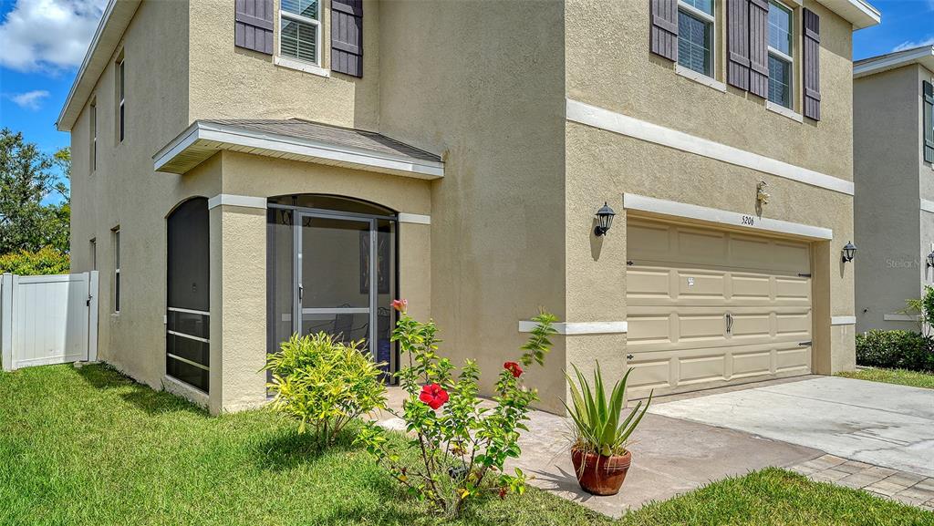 A two-story tan house with a screened front entryway, garage, and a small front garden — 5206 WILLOW BREEZE WAY, PALMETTO, FL