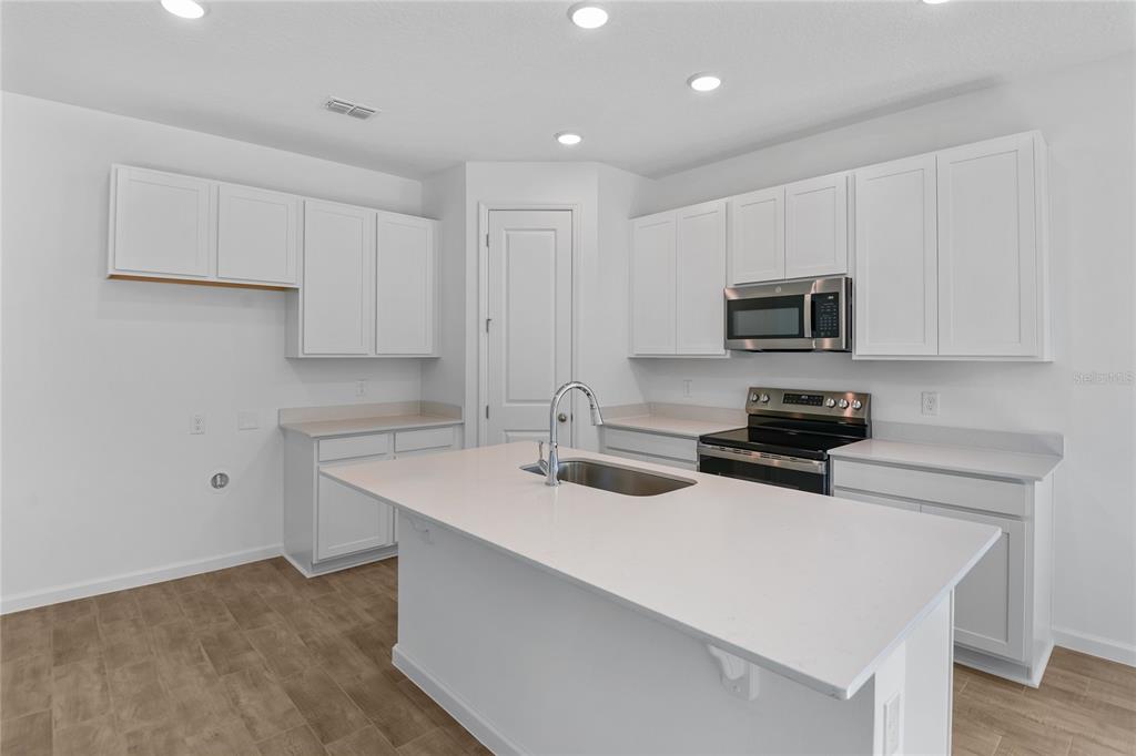 A modern kitchen features white cabinets, a central island with a sink, and stainless appliances — 6182 SW 64TH TERRACE, OCALA, FL